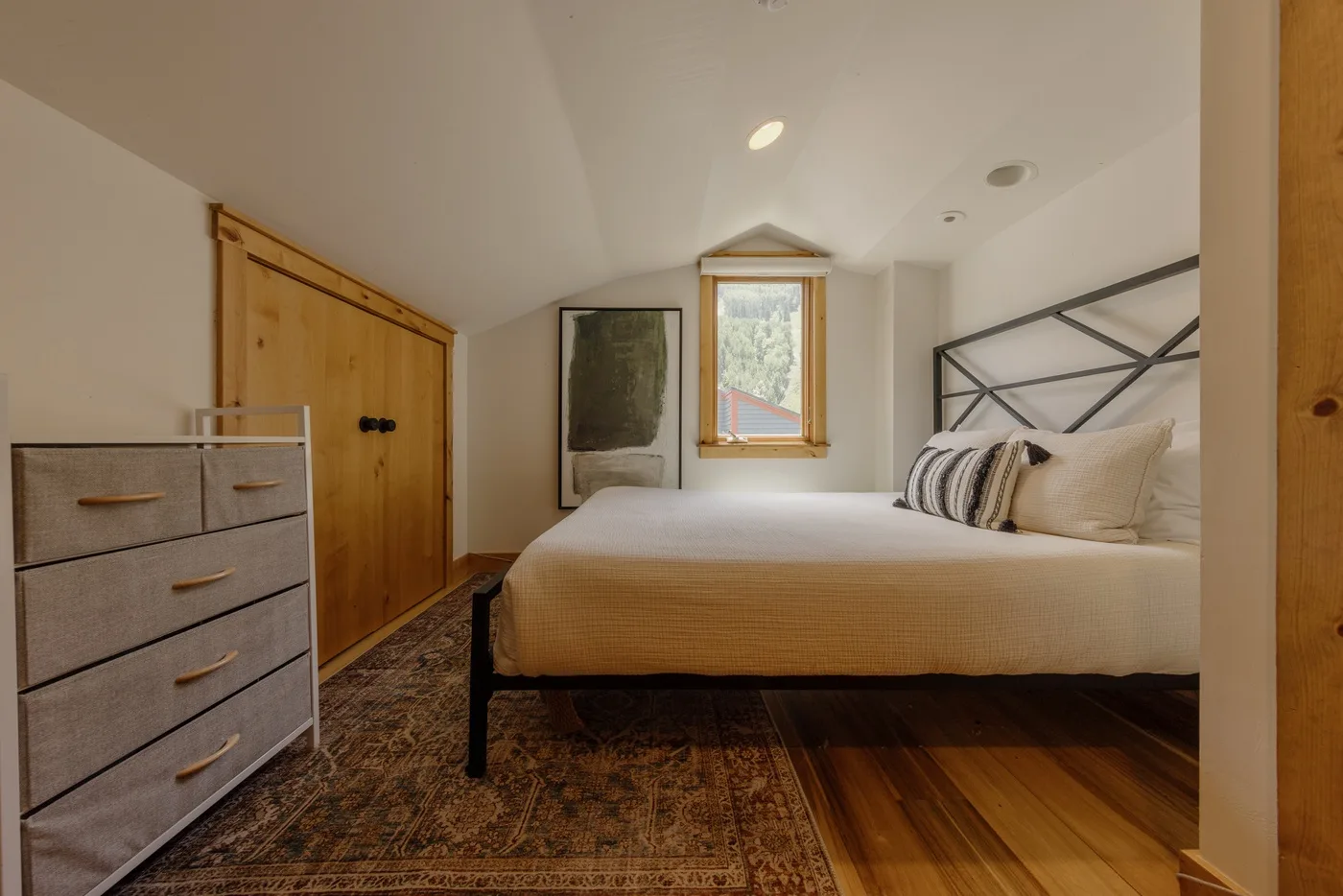 Un dormitorio con una cama bajo un techo inclinado y una ventana pequeña.