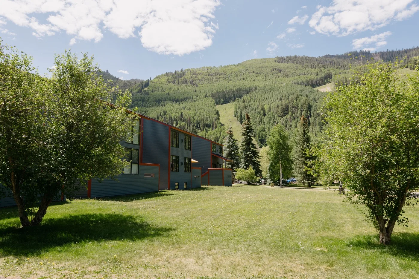 Un edificio moderno se encuentra junto a un césped abierto, con colinas boscosas al fondo.