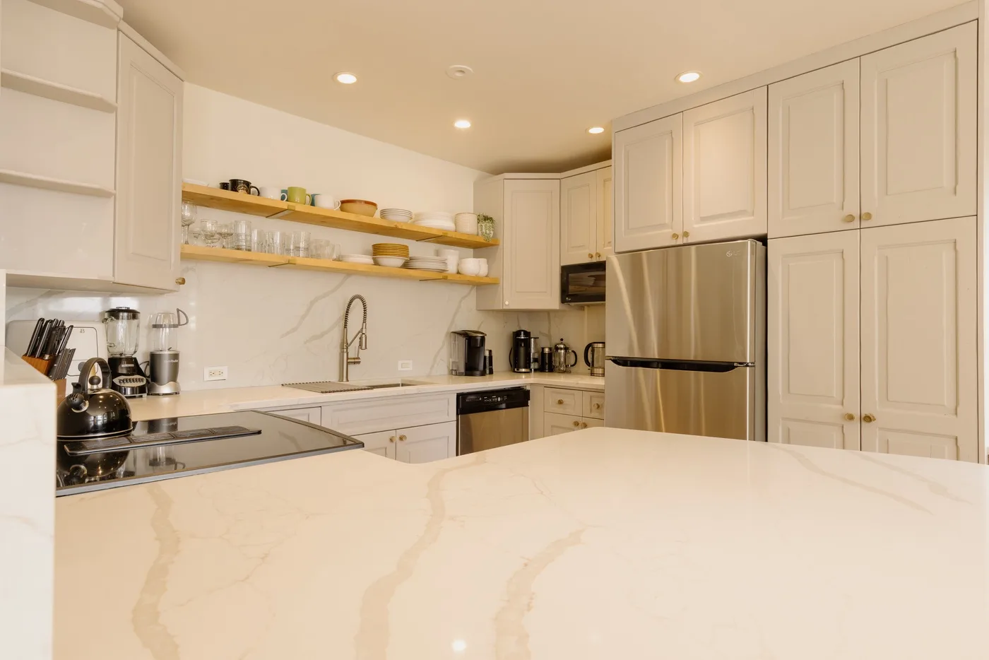 Una cocina luminosa con una amplia encimera, refrigerador de acero inoxidable y estantes abiertos.