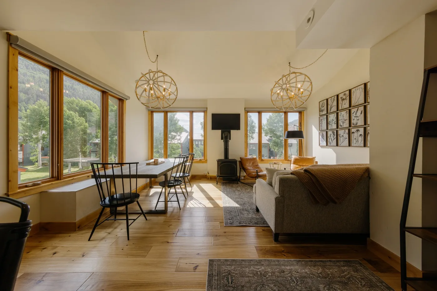 Una sala luminosa con grandes ventanas, asientos y una mesa de comedor.