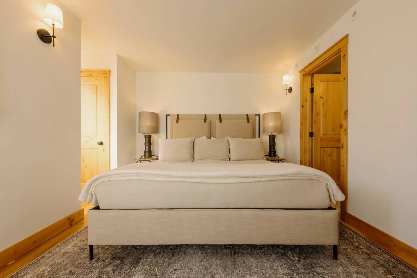 Un dormitorio con una cama bien tendida, lámparas de noche y puertas de madera.
