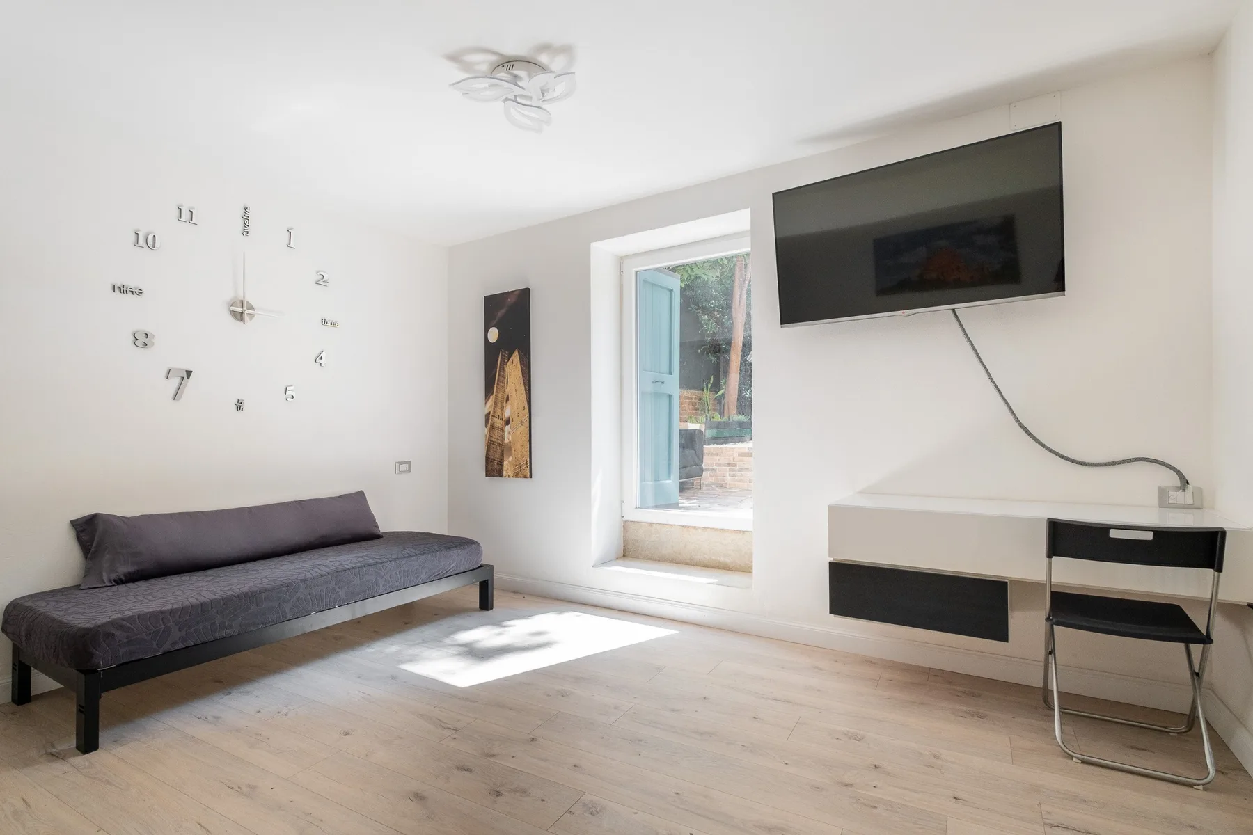 Una sala luminosa con una cama de día, un televisor en la pared y una ventana abierta.