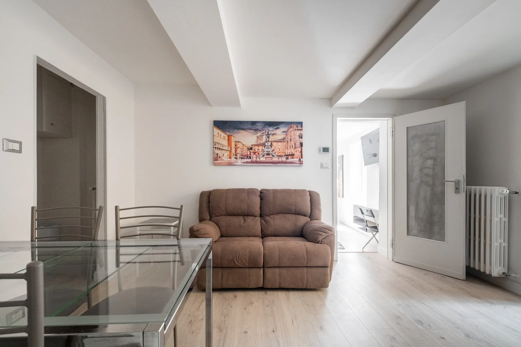 Una sala de estar con un sofá marrón, una mesa de centro de vidrio y una puerta abierta.