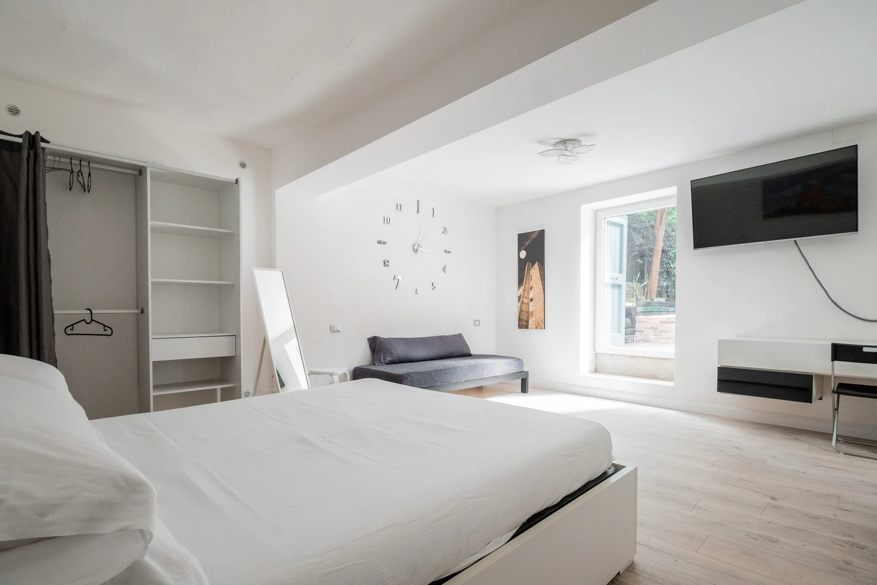 A bright bedroom with a large bed, a sofa, and a wall-mounted television.