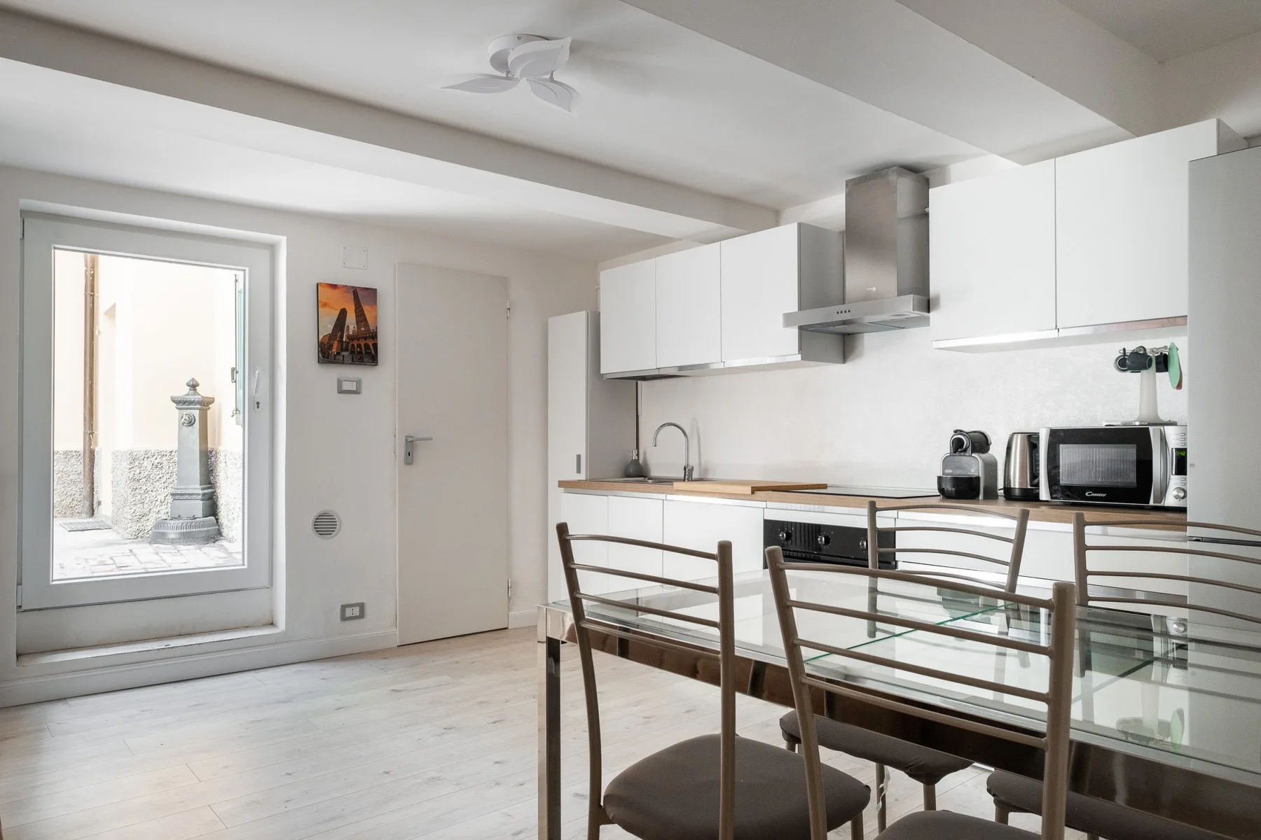 Una luminosa cocina y comedor con armarios blancos y una mesa de cristal.