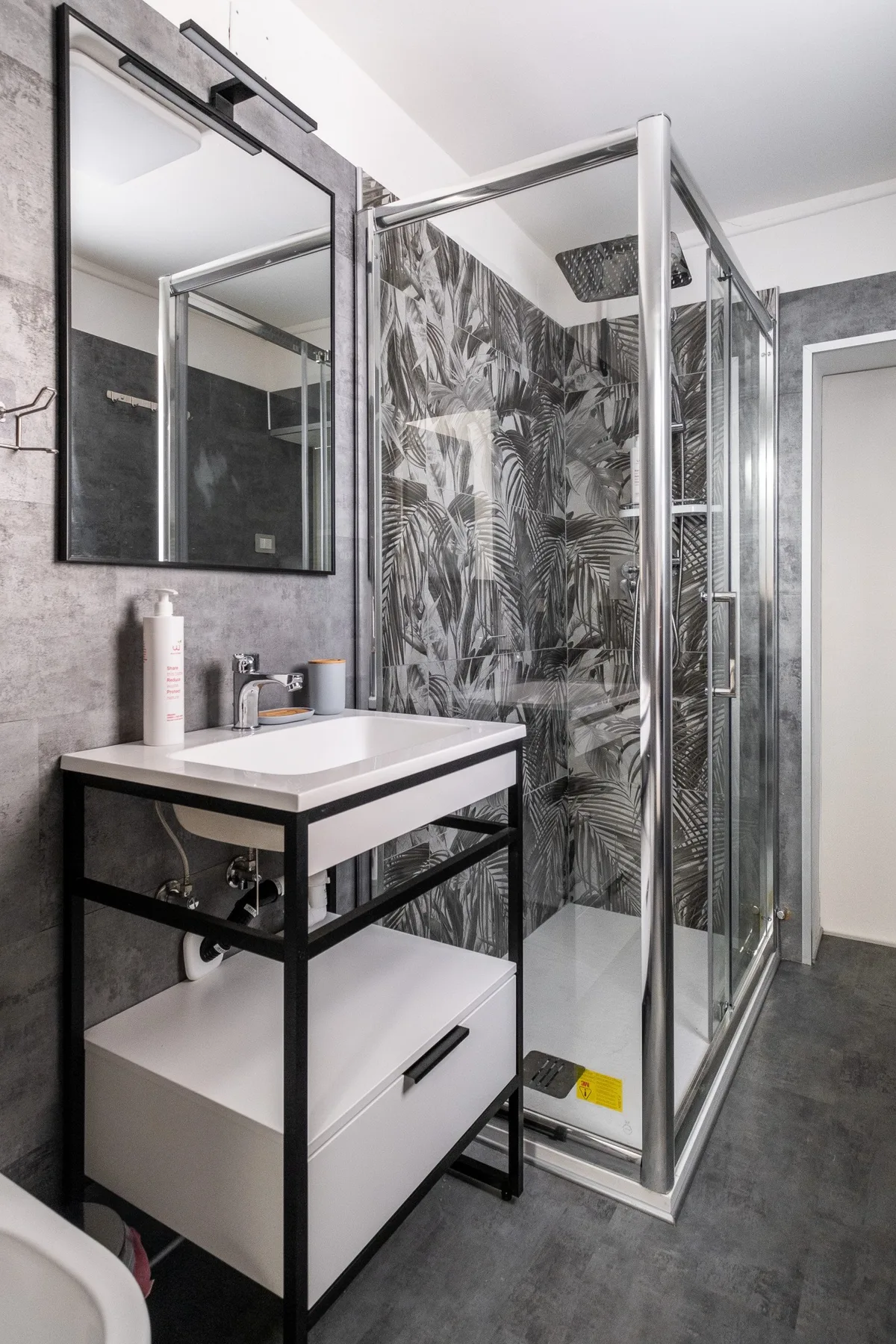 Un baño con tocador y una ducha de vidrio con paredes de estampado vegetal.