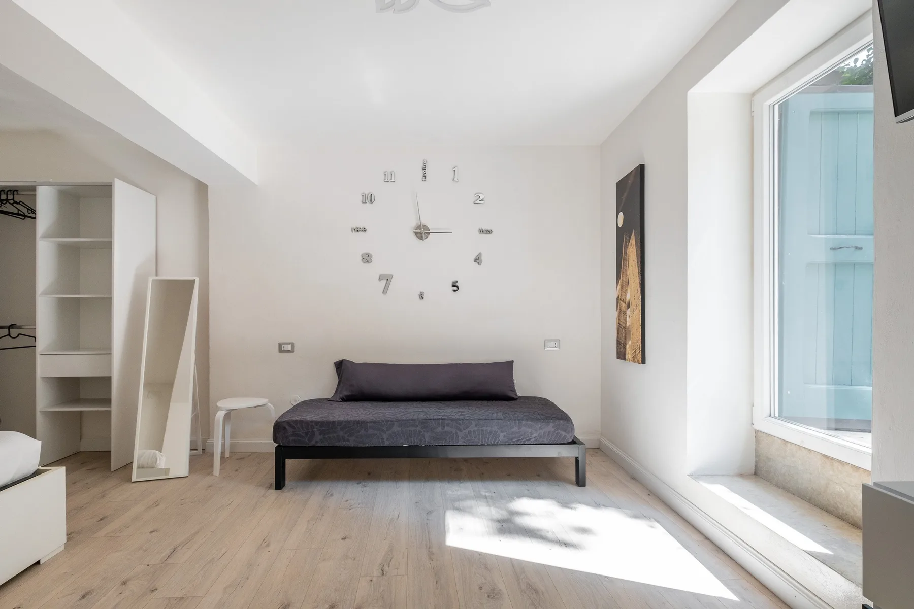 Un dormitorio luminoso con una cama baja bajo un gran reloj de pared.