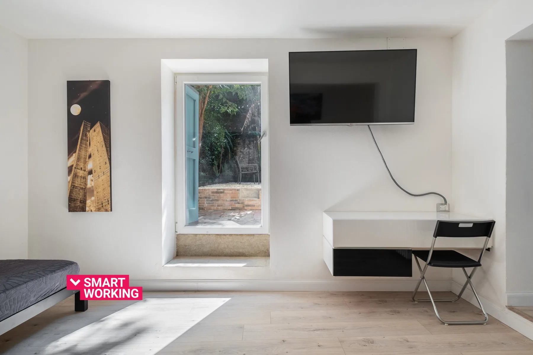 A bright bedroom with a wall-mounted television and a desk by the window.