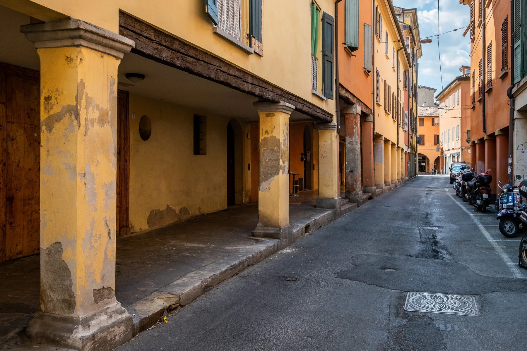 Una calle estrecha pasa entre edificios coloridos, con scooters estacionados junto a la acera.