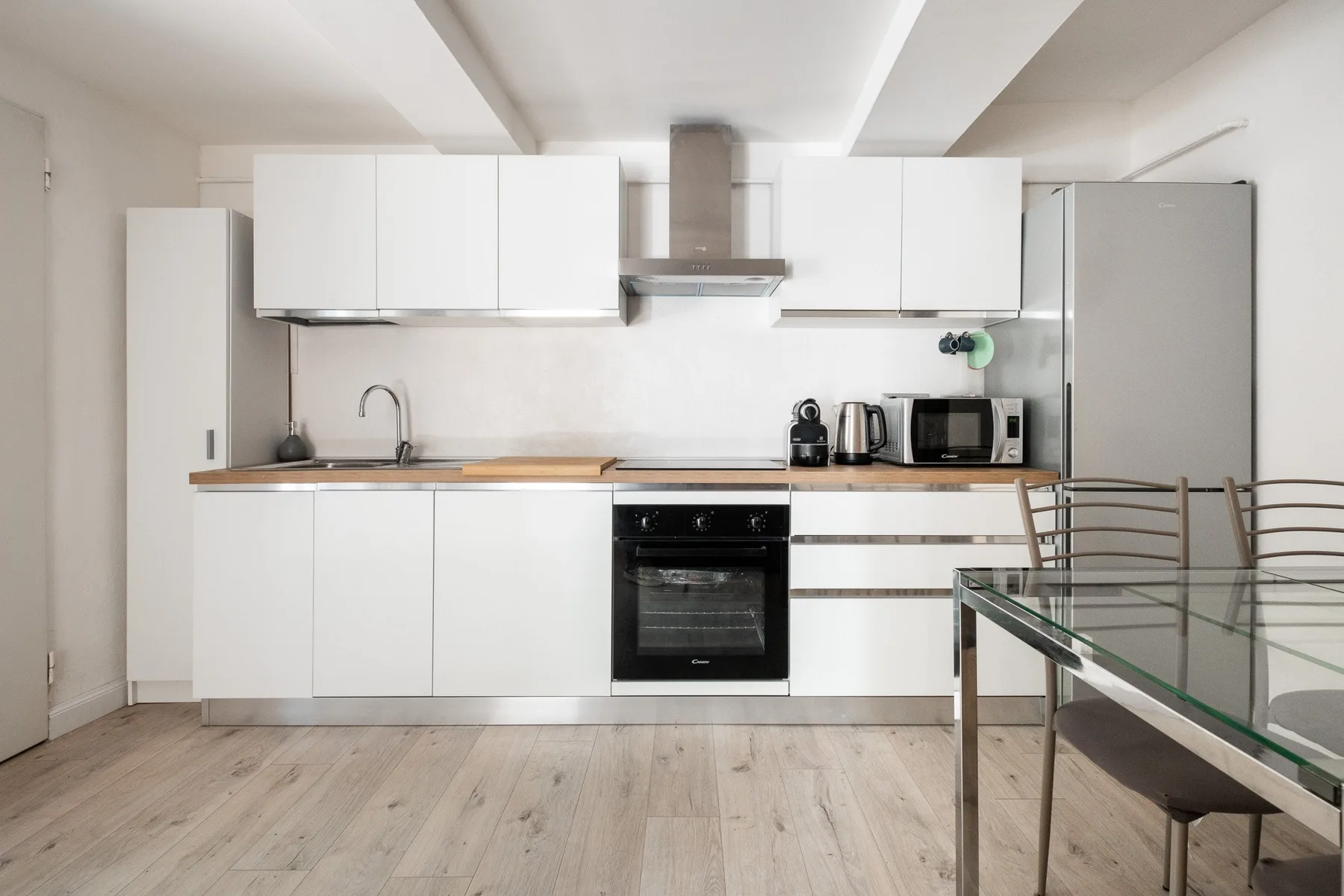 Una cocina moderna con gabinetes blancos, electrodomésticos y una mesa de comedor de vidrio.