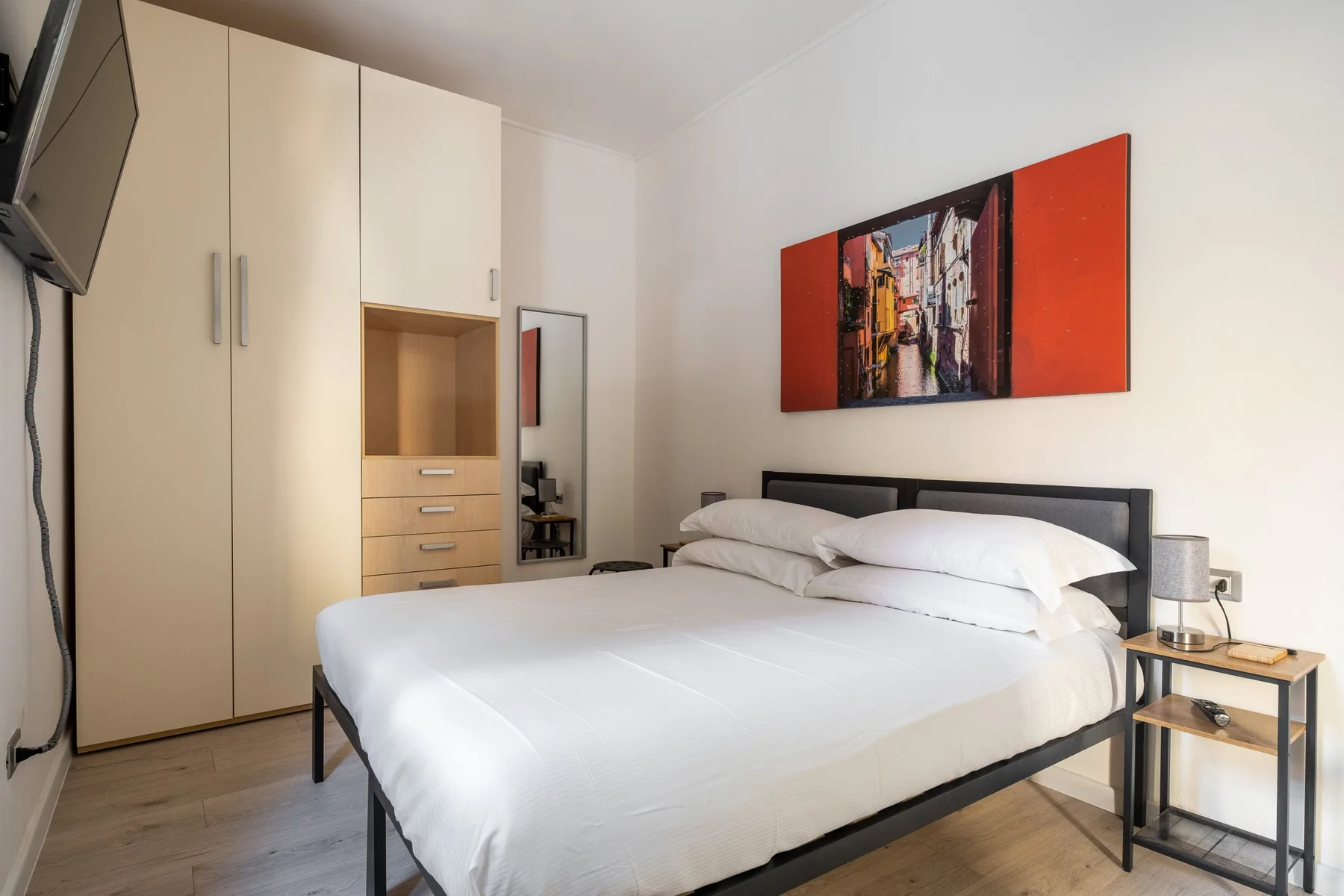 A bedroom with a large bed, built-in wardrobes, and colorful wall art.