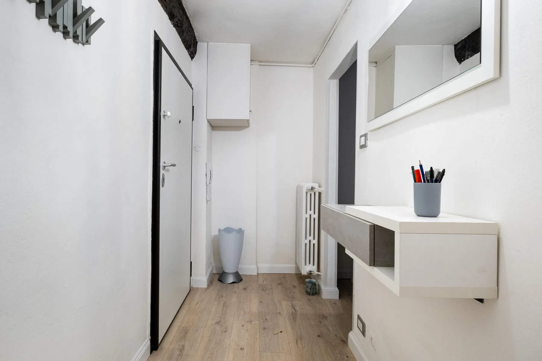 Una entrada luminosa con una puerta, ganchos de pared y una consola flotante bajo un espejo.