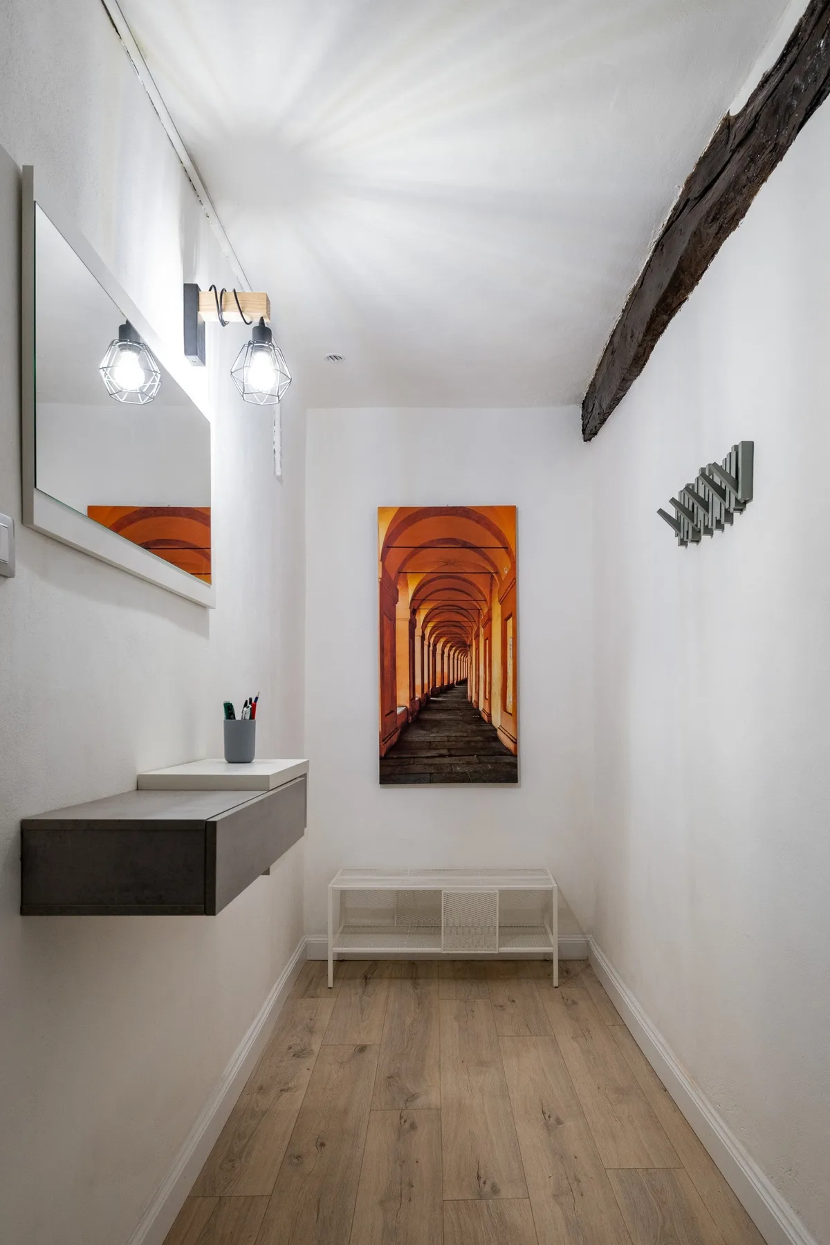 Un pasillo estrecho con suelo de madera, arte en la pared y un pequeño banco.