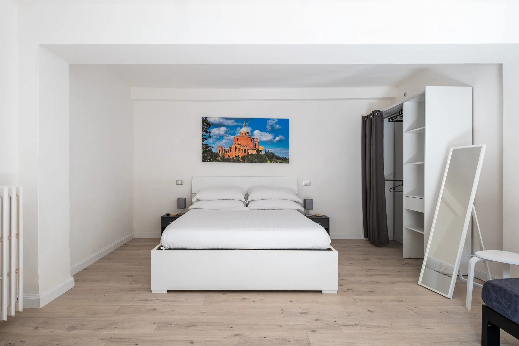 Un dormitorio luminoso con una cama bien tendida y una colorida obra de arte encima.