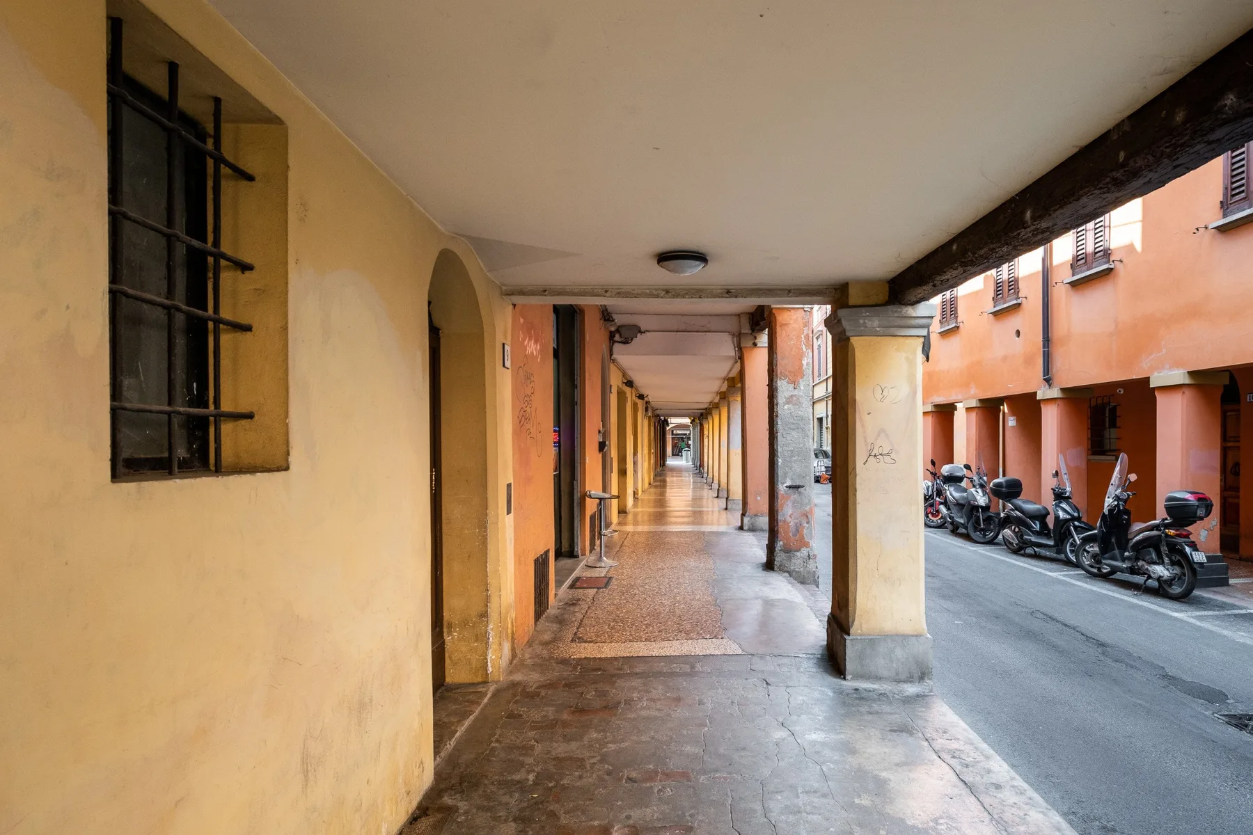 Un paseo cubierto recorre una calle junto a edificios coloridos y motos estacionadas.