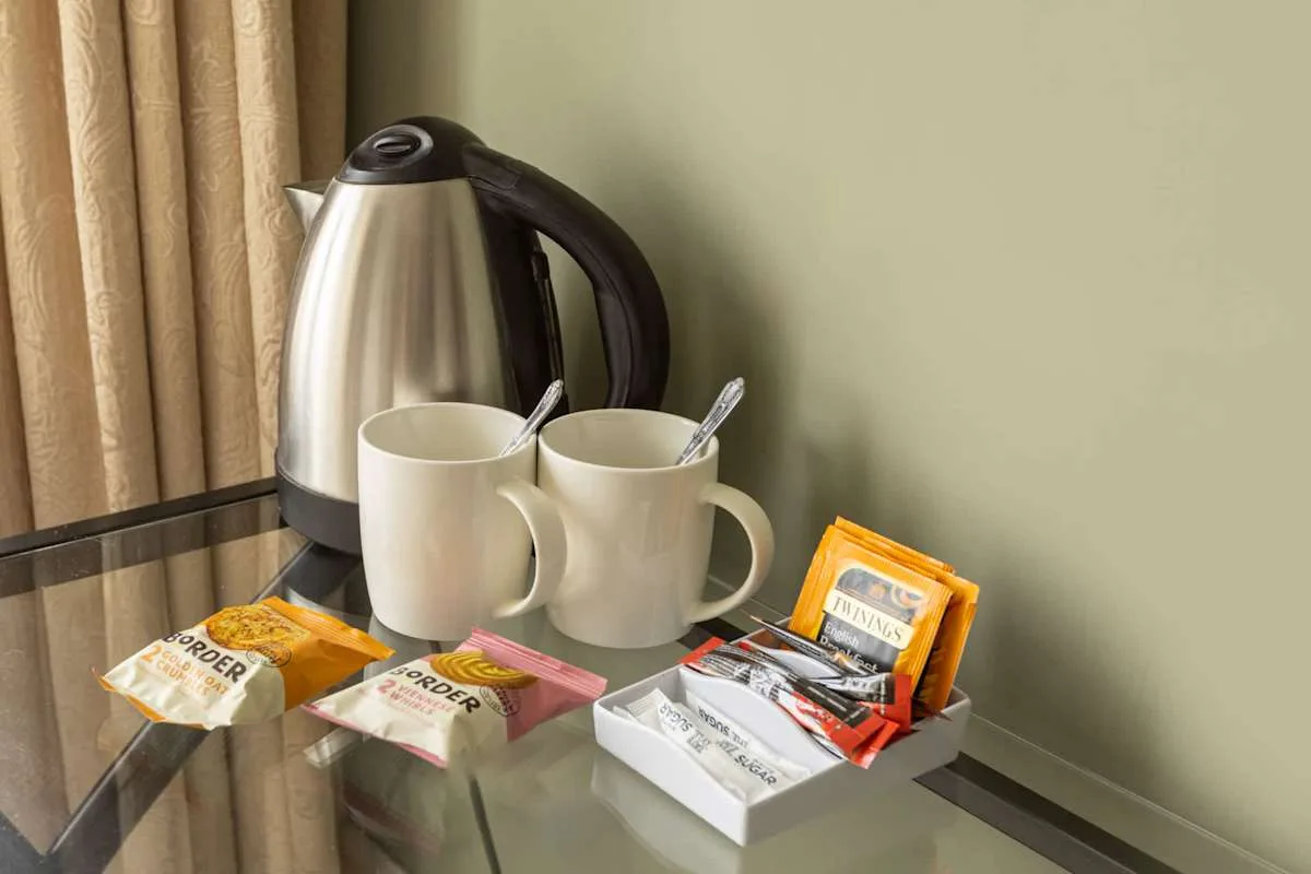 A glass-topped table holds a kettle, two mugs, and packets of tea and coffee.