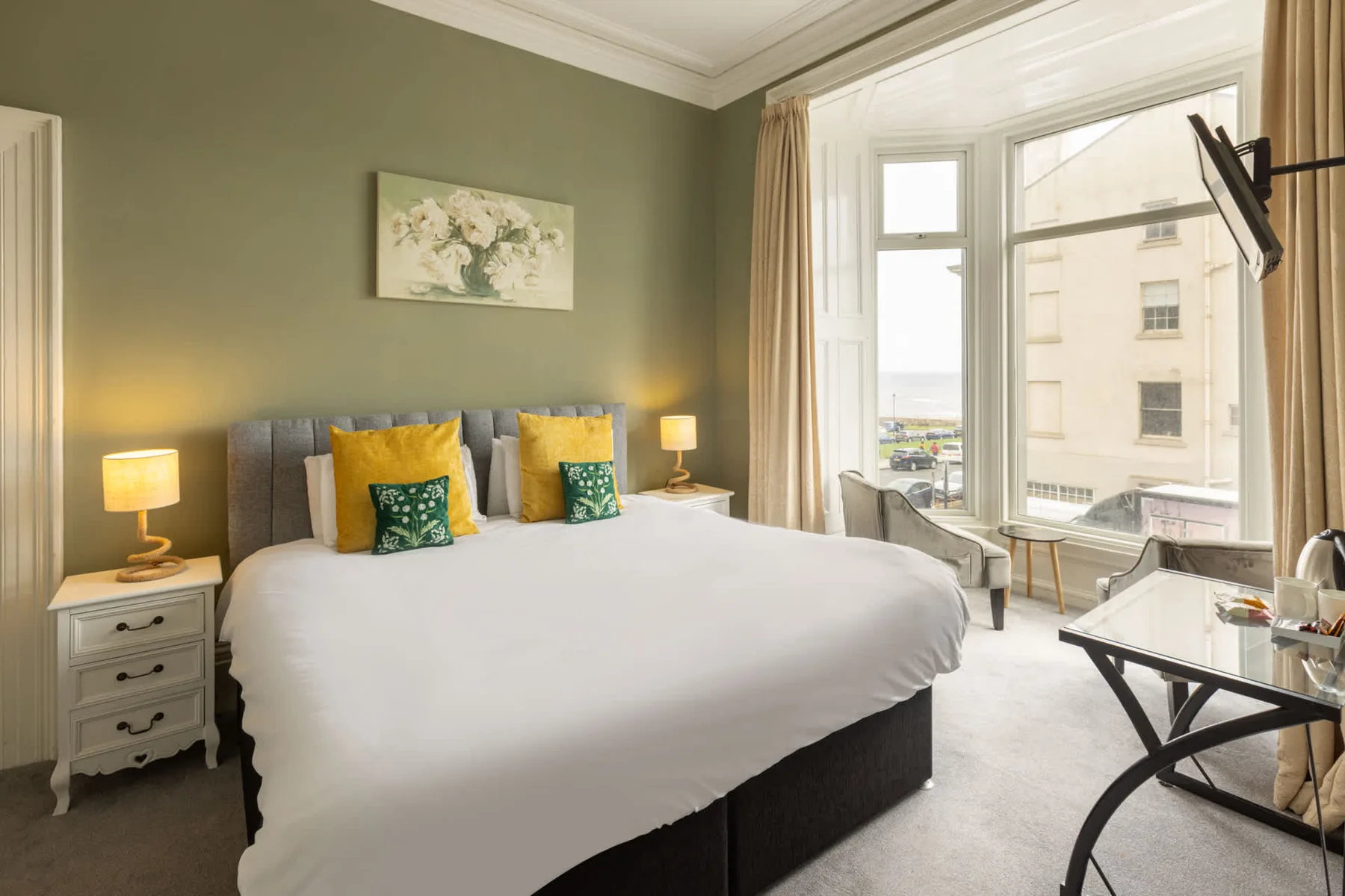A bedroom with a neatly made bed, green walls, and large windows.