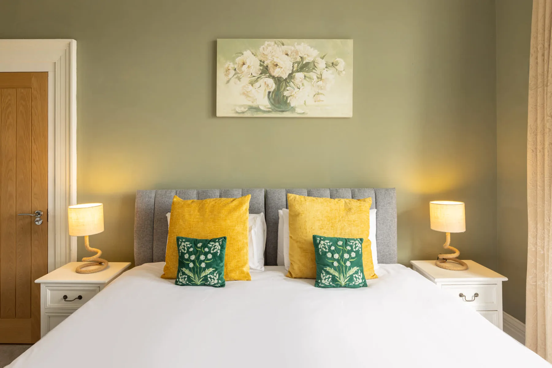 A bedroom with a neatly made bed, colorful cushions, and matching bedside tables.