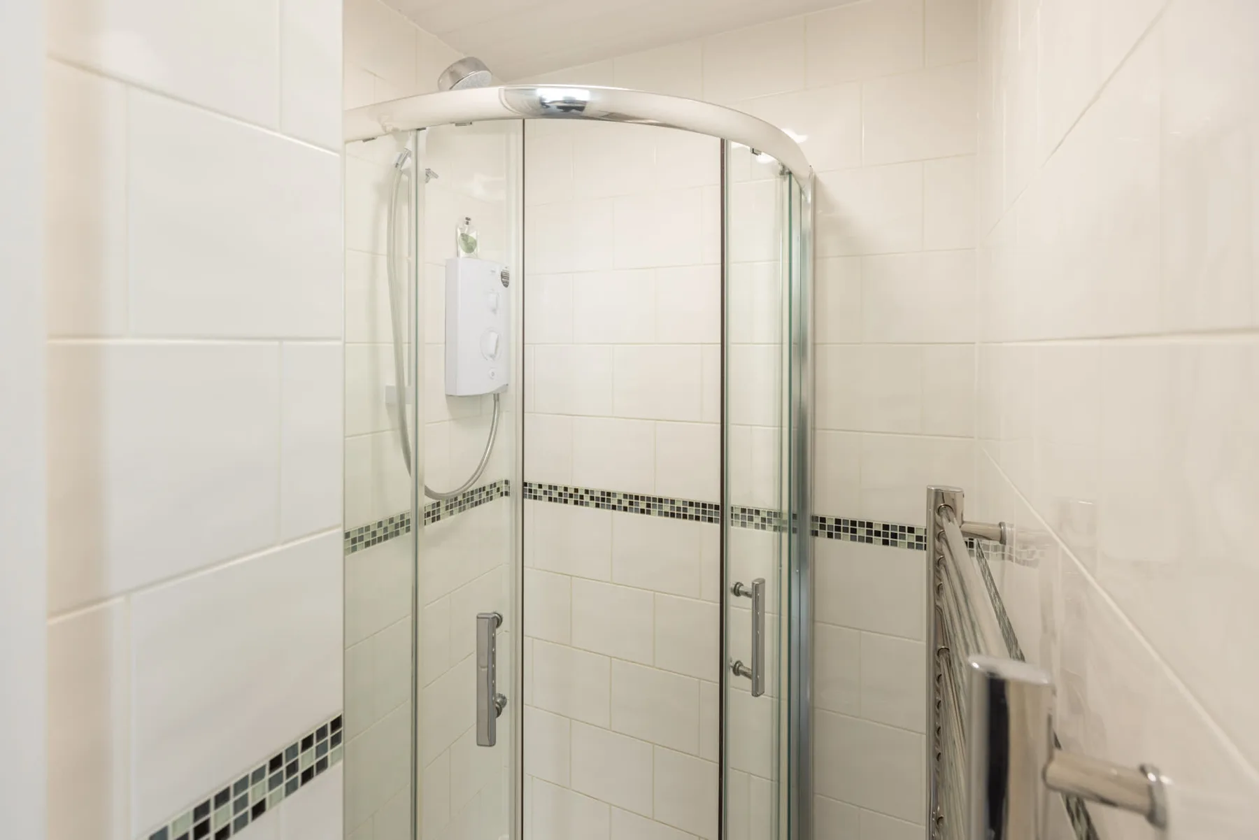 A tiled bathroom with a glass shower and a decorative wall border.