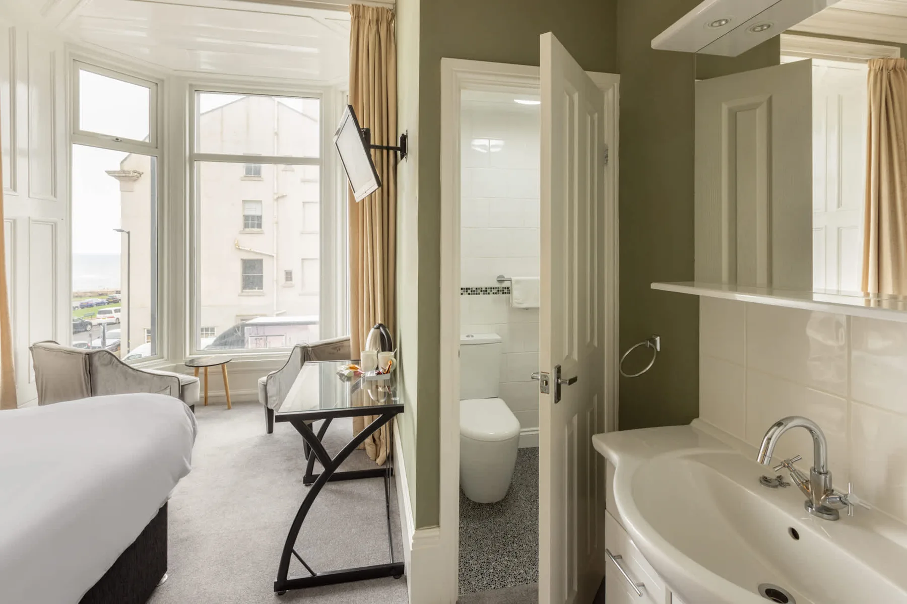 A bedroom with a large window and a bathroom visible through the open doorway.