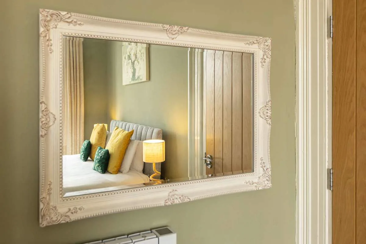 A bedroom is reflected in a large framed wall mirror.