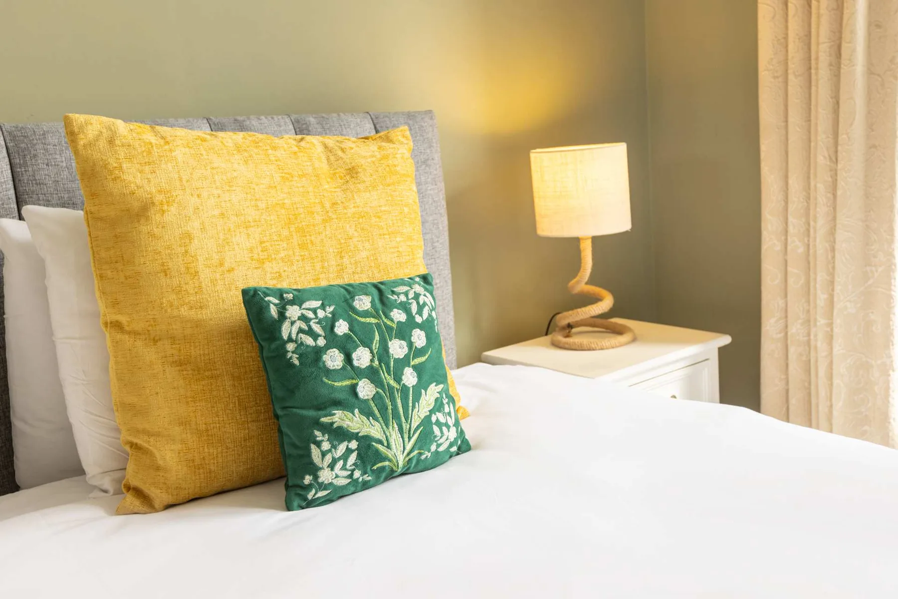 Bedroom with a neatly made bed and a lit bedside lamp.