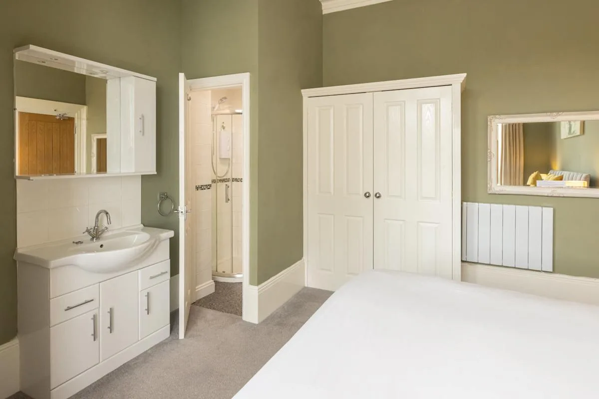 A bedroom with a white bed, built-in cupboards, and a sink beside the doorway.