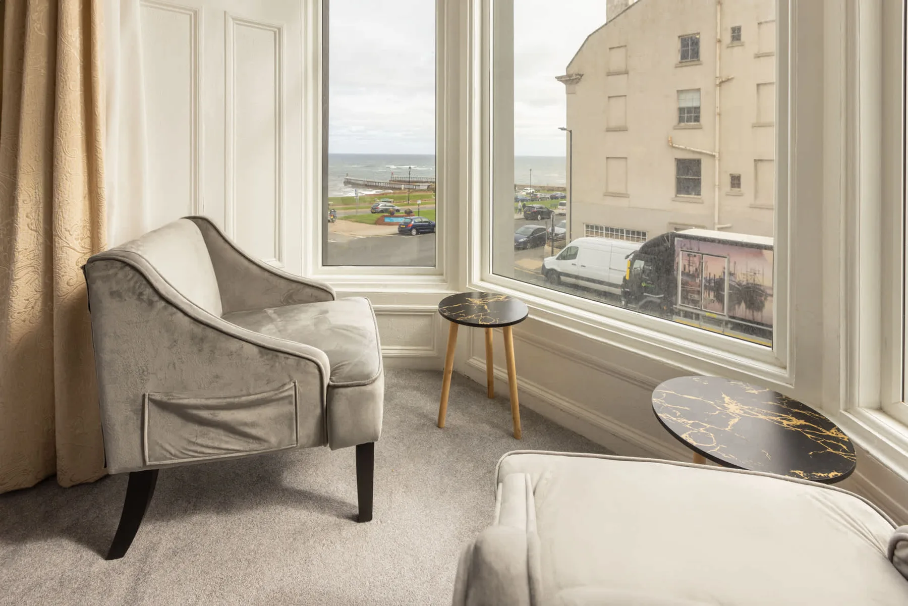 A bright sitting area with upholstered seating and large windows overlooking the street.