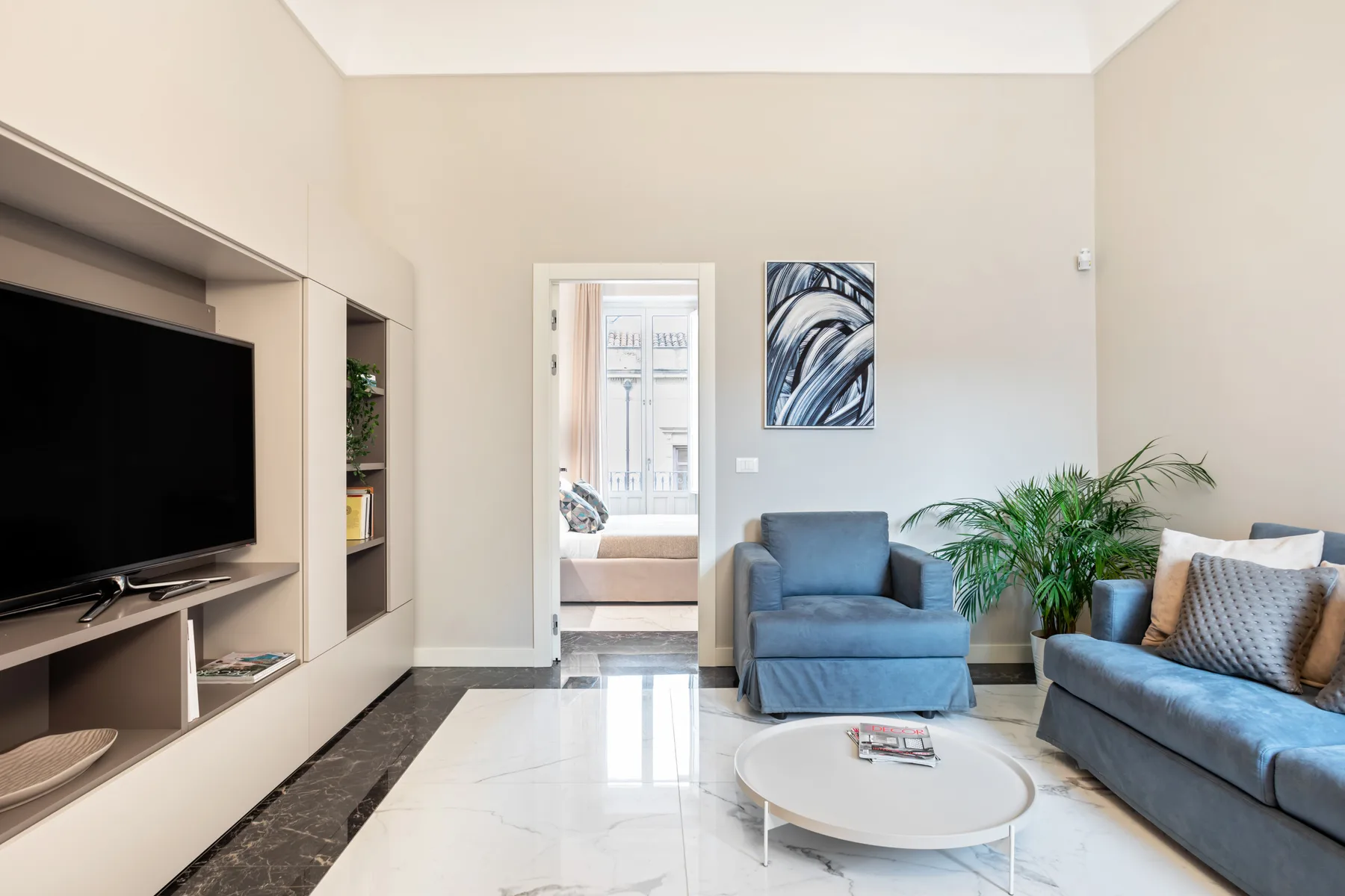 Una sala luminosa con asientos azules, un televisor y una planta en maceta.