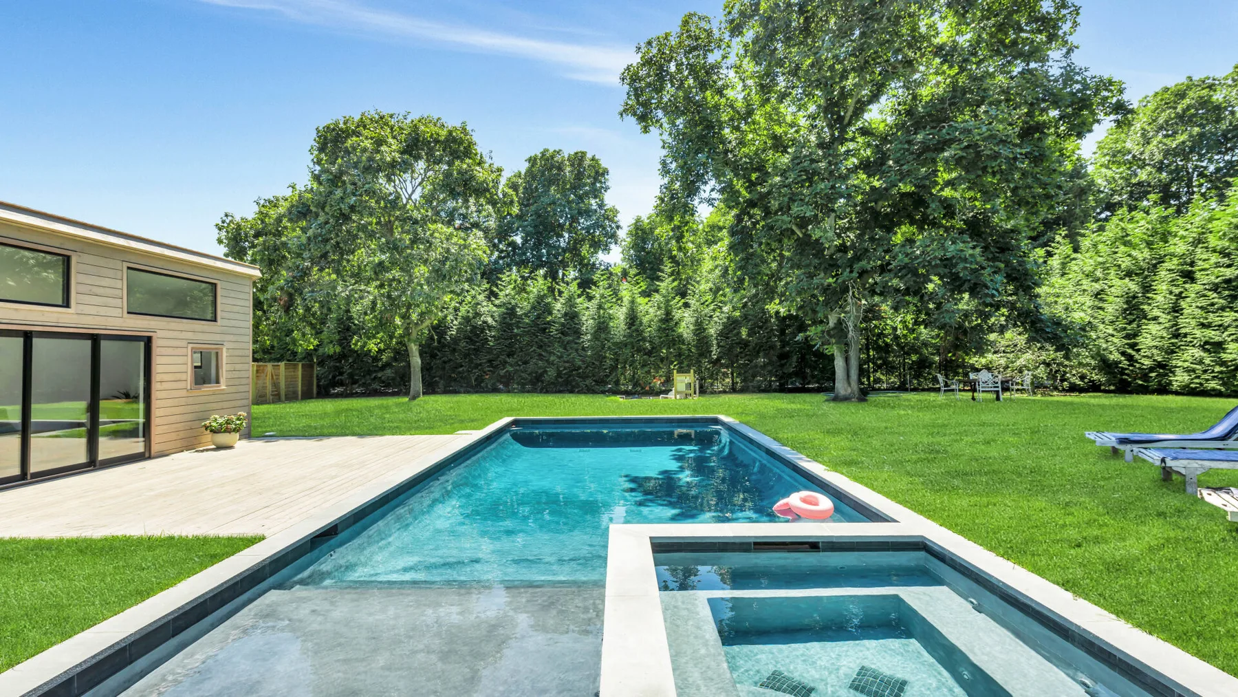 A backyard swimming pool sits beside a modern house and a broad green lawn.