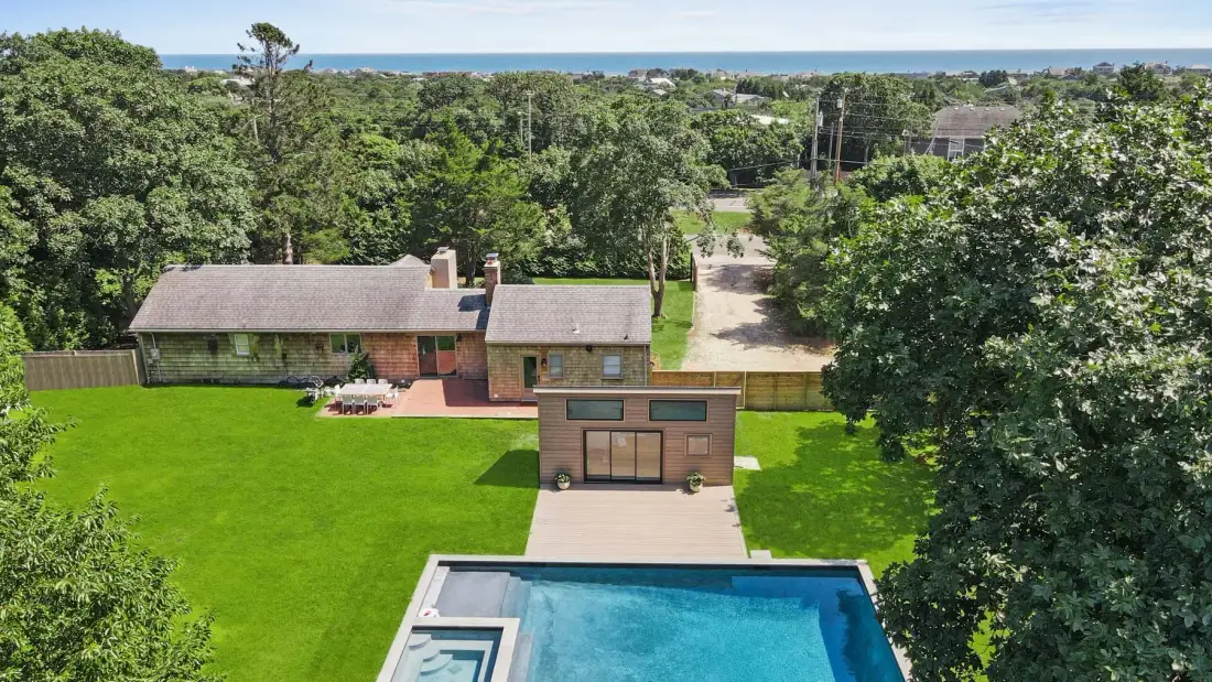 An aerial view shows a house, a swimming pool, and a broad green lawn.