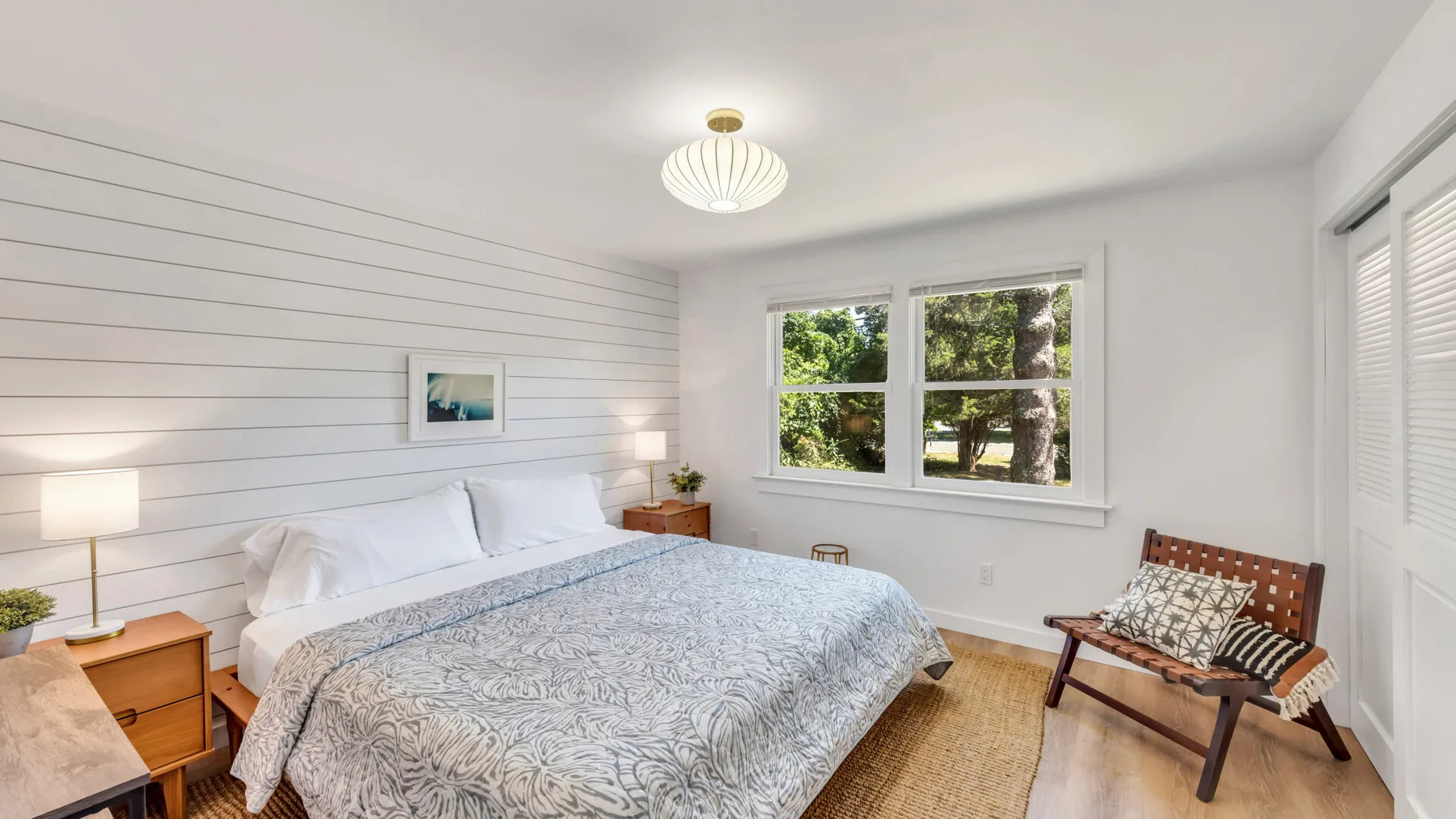 A bright bedroom with a large bed, windows, and a small seating area.