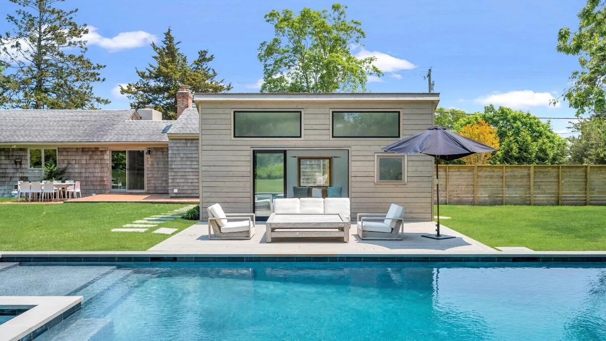 A backyard pool in front of a modern pavilion with outdoor seating.