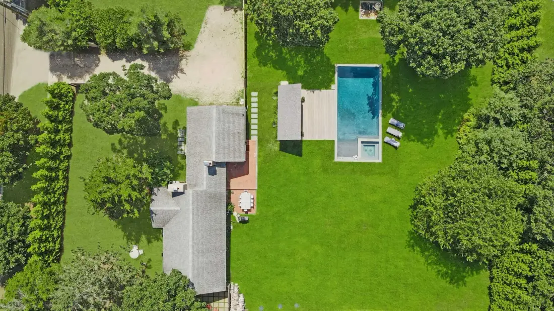 An aerial view shows a house beside a swimming pool and green lawn.