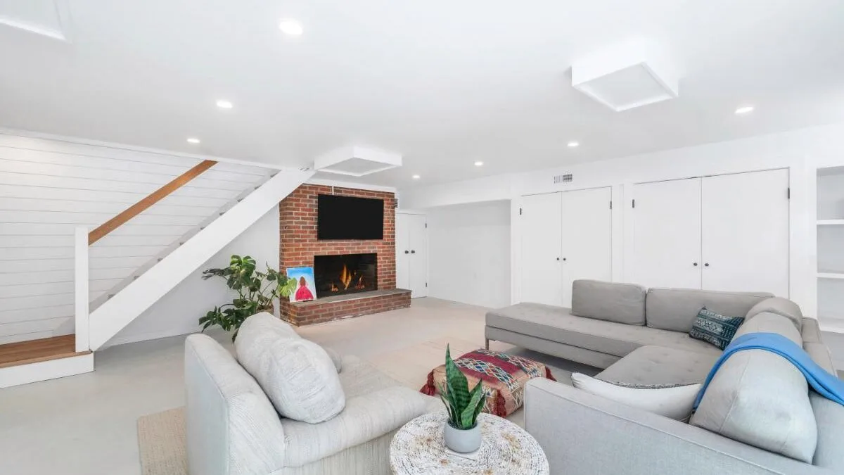 A bright living room with sectional seating, a brick fireplace, and a staircase.