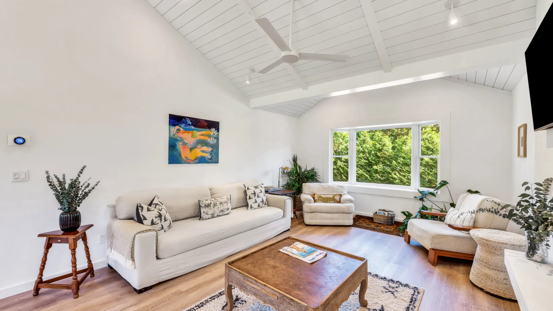 A bright living room with light seating, a wooden coffee table, and large windows.