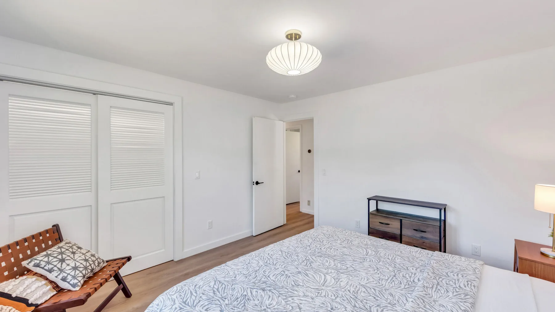 A bright bedroom with a bed, shuttered windows, and a small dresser.