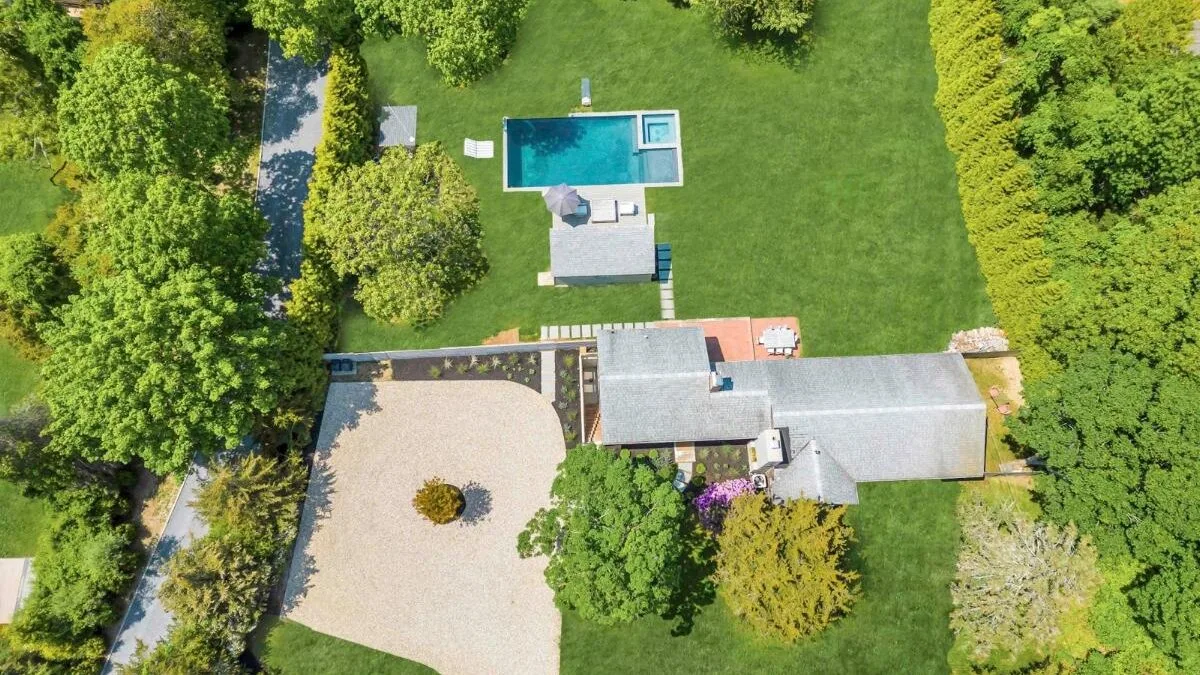 Aerial view of a landscaped property with a rectangular swimming pool and paved courtyard.