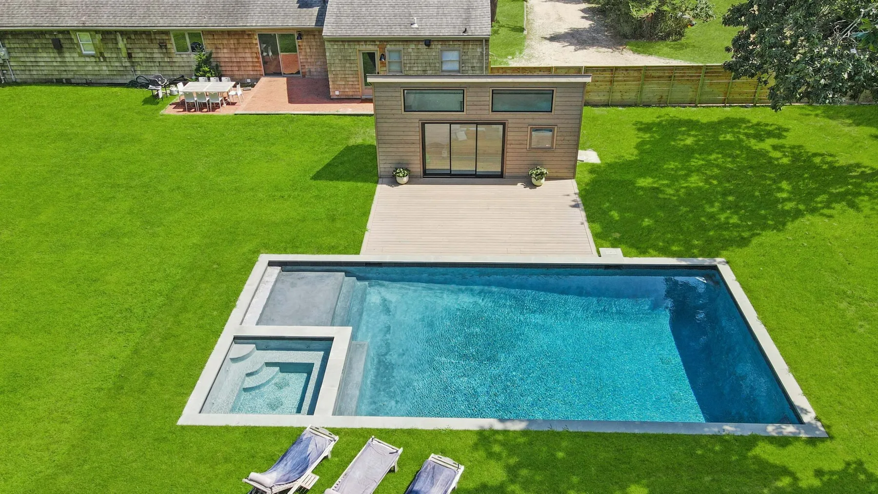 An outdoor swimming pool sits beside a lawn and a modern building.