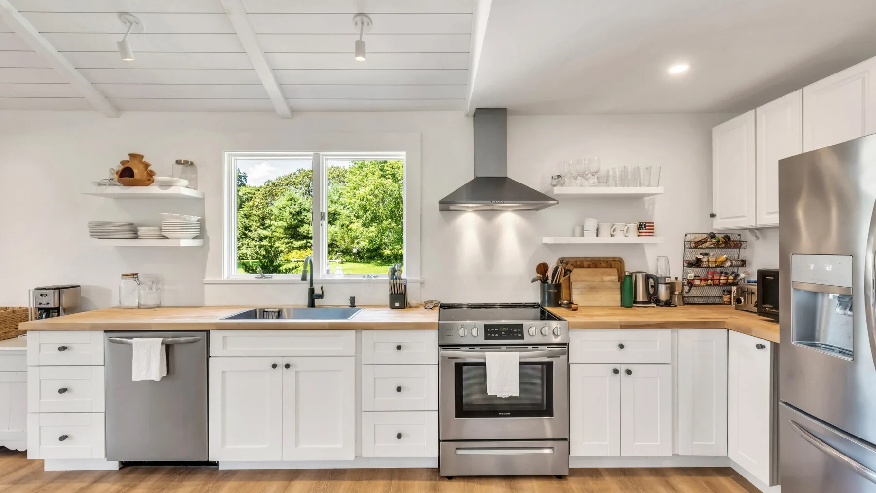 A bright kitchen with white cabinetry, a central range, and a large window.