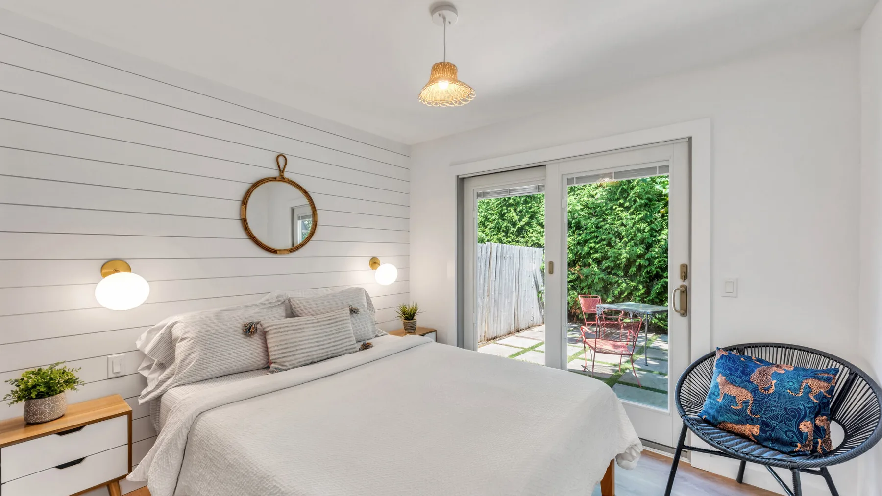 A bright bedroom has a bed, wall mirror, and glass doors opening to a patio.