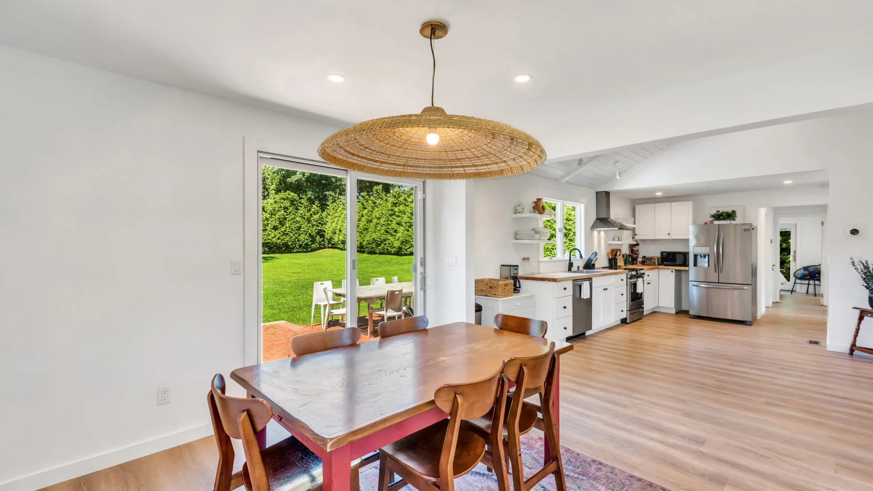 A dining area with a wooden table opens onto a bright kitchen and garden.