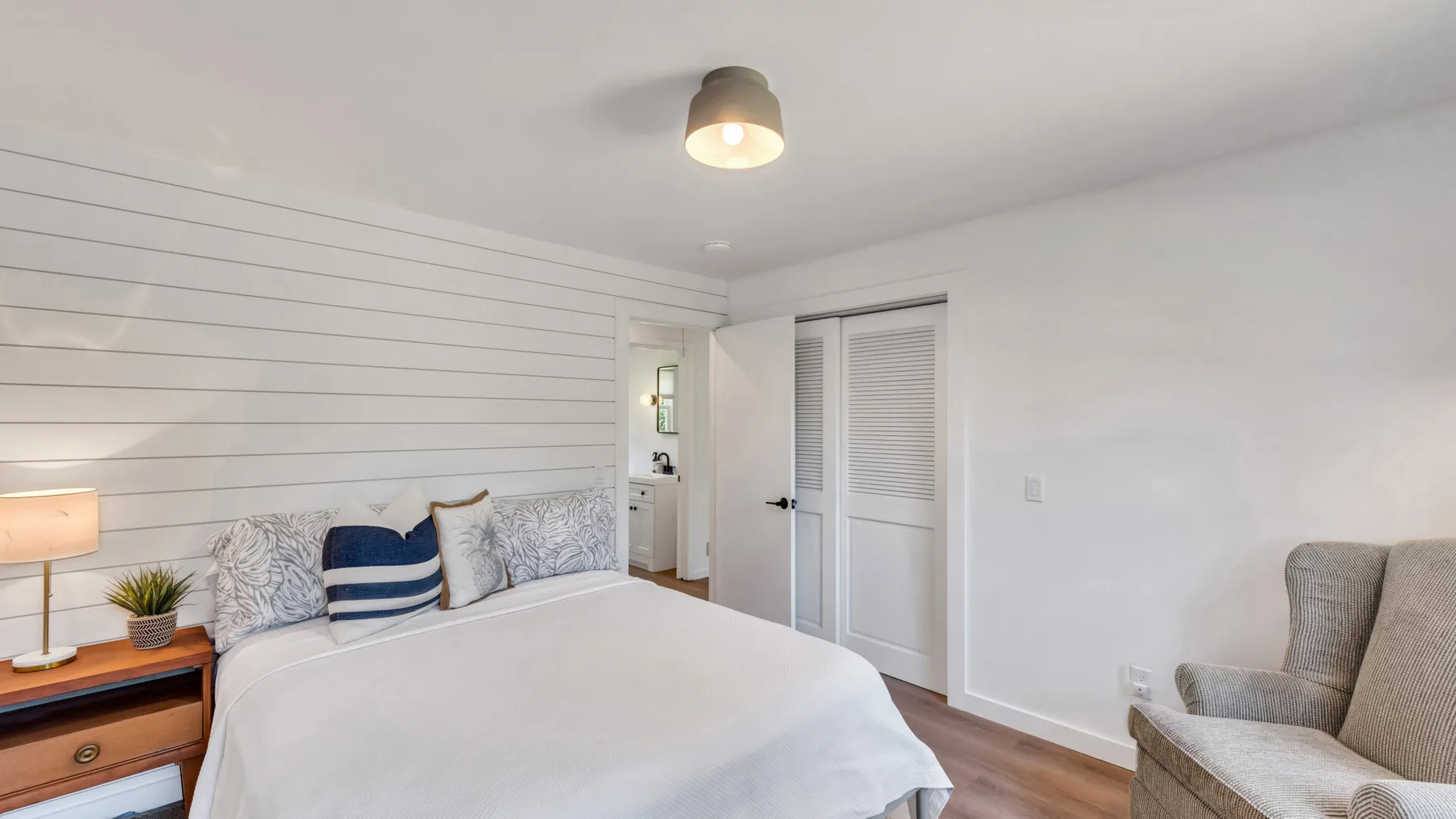 A bright bedroom with a neatly made bed and a bedside table.