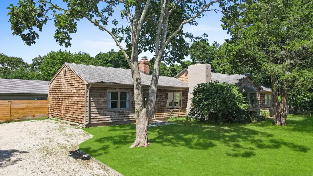 A low house stands beside a green lawn and mature trees.
