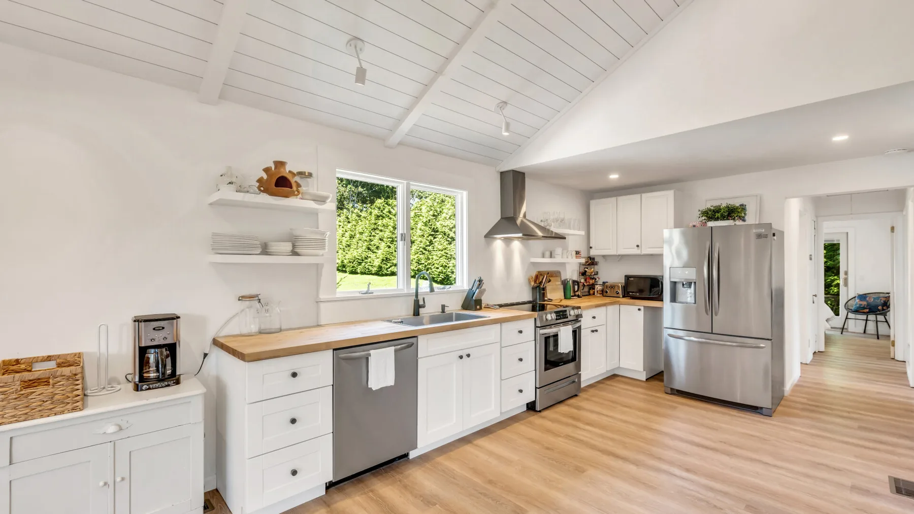 A bright kitchen with white cabinets, stainless steel appliances, and a wood countertop.