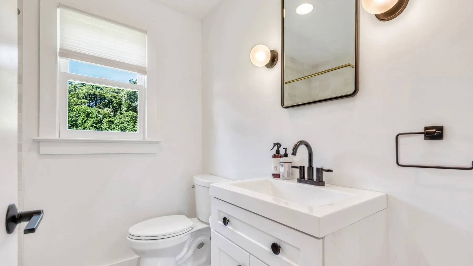 A bright bathroom with a sink, toilet, and window.