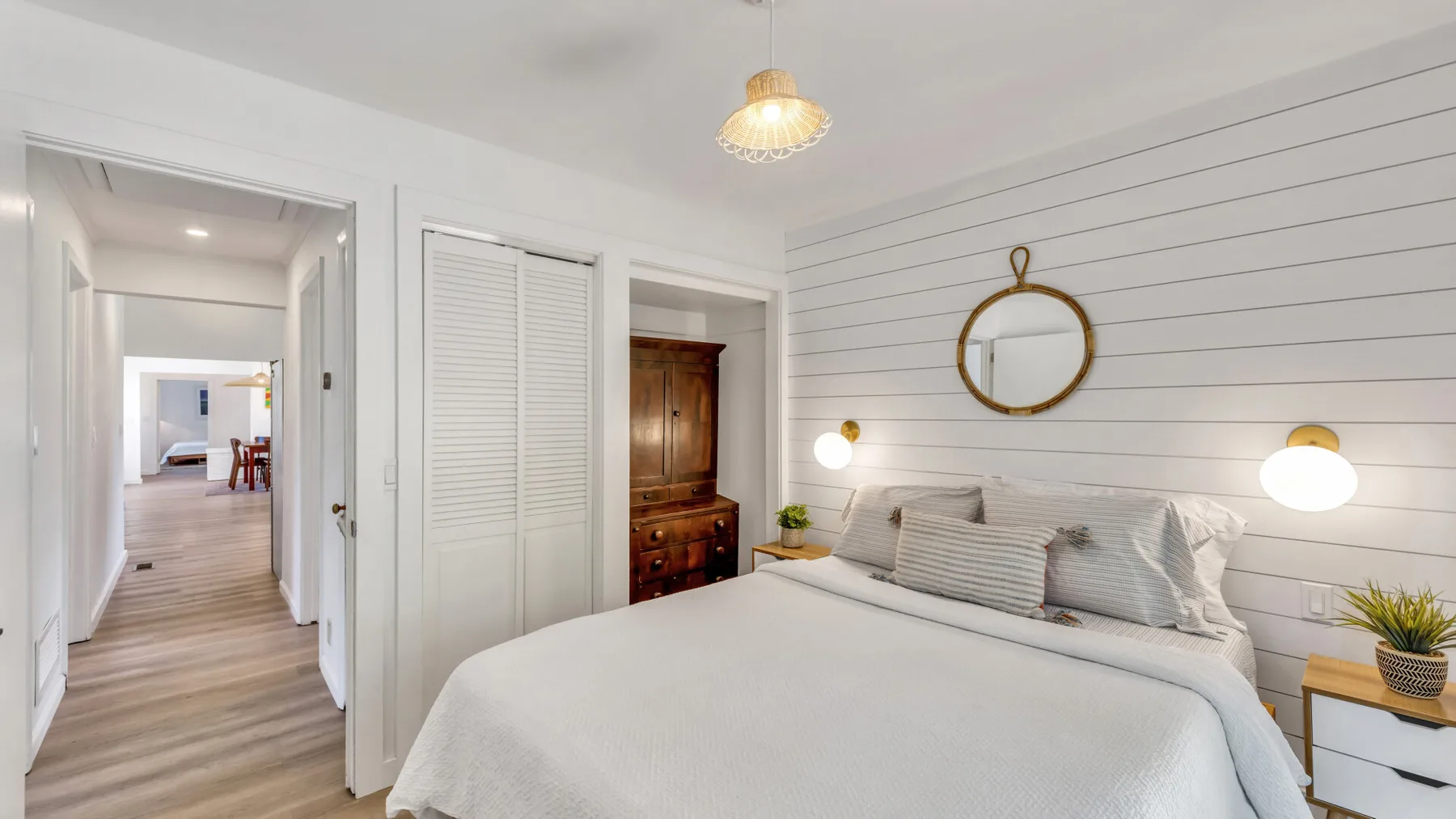 A bedroom with a neatly made bed, wall lights, and a round mirror.