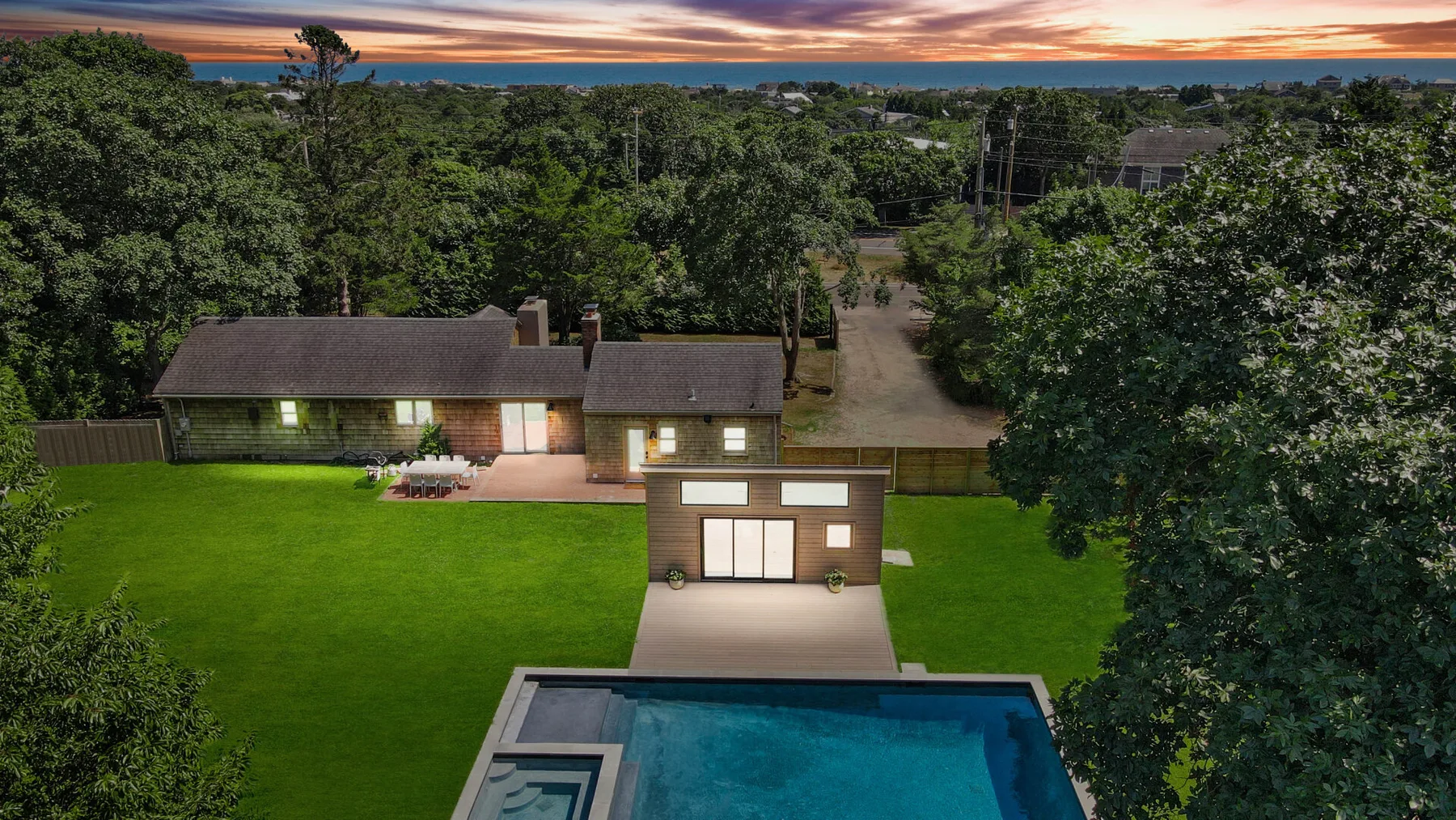 An aerial view shows a lit house beside a lawn and swimming pool at dusk.