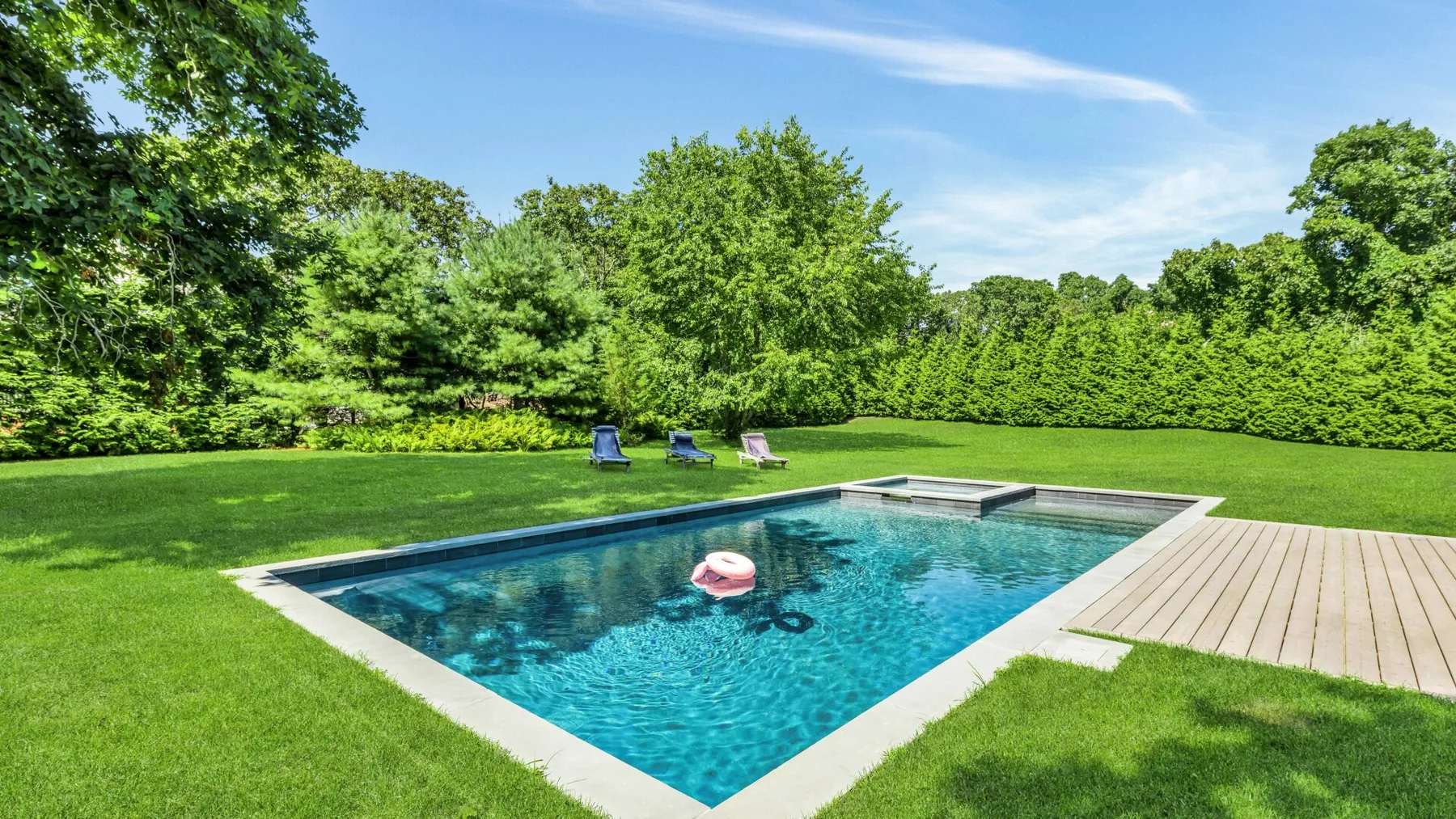An outdoor swimming pool sits in a grassy lawn surrounded by leafy trees.