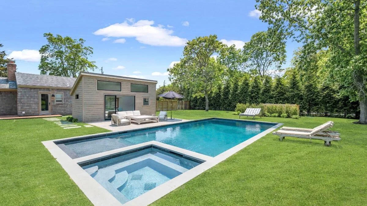 A backyard pool and attached shallow basin sit beside a modern house.